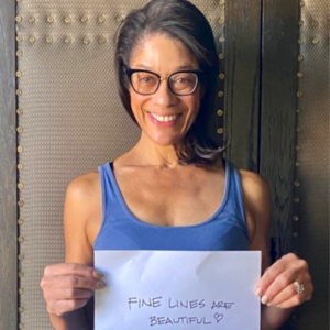 woman holds up sign that says fine lines are beautiful