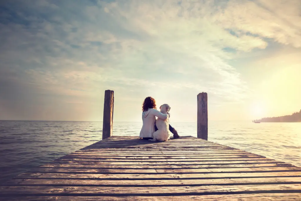 woman embracing sweetly his dog while looking the view of lake