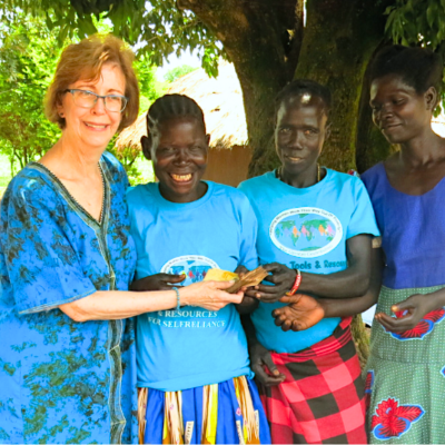 Karon Wright in a blue dress is standing with three other women under a tree, giving out a micro loan
