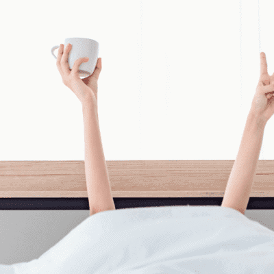 Woman greets morning with hands peeking out from bedsheets