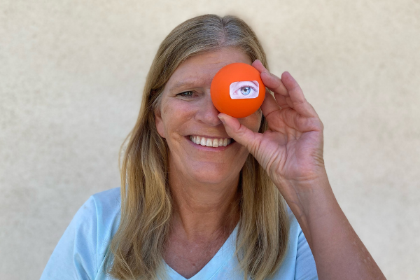 Woman holding orange ball at eyesight with an image of an eye on it