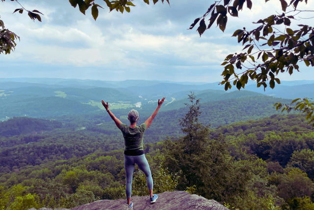 female standing at mountain top with arms extended