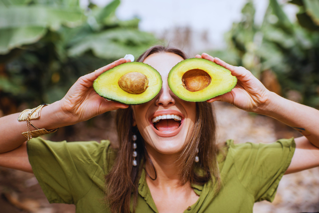 Woman holding avocado halves to her eyes like glasses 