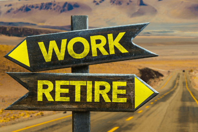 A road in a desert with two directional signs pointing opposite ways labeled "WORK" and "RETIRE" in yellow letters.
